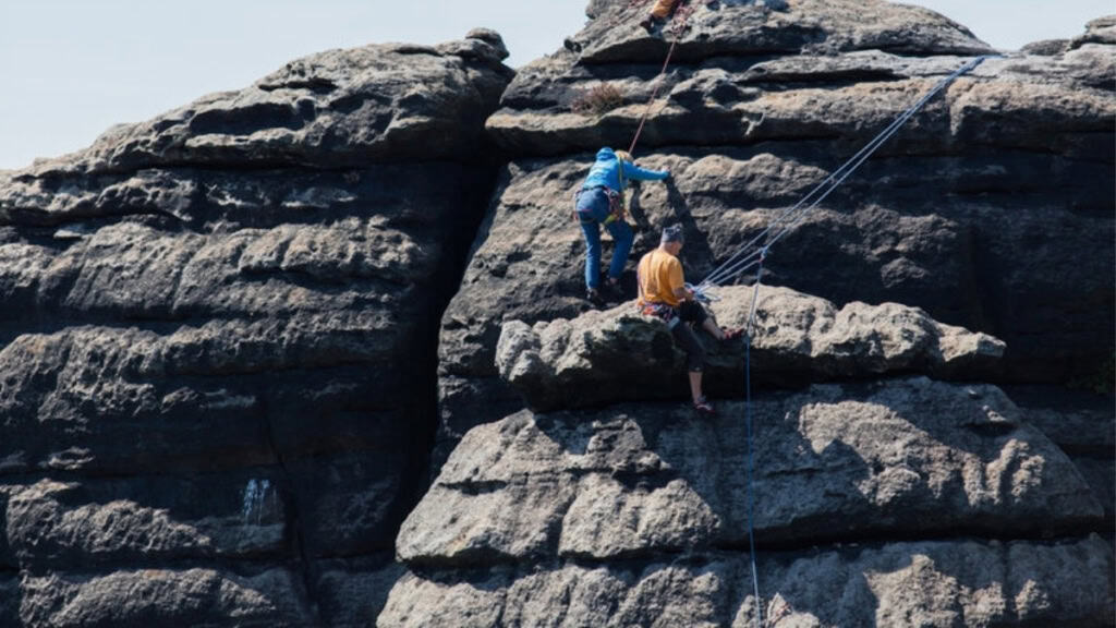 Zwei Bergsteiger sind kurz davor die Spitze eines Sandstein Felsens zu erklimmen.
