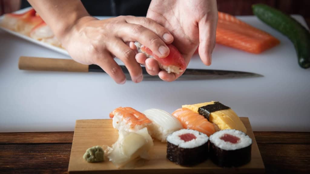 Ein Sushi Stück wird auf eine Sushi Platte gelegt.