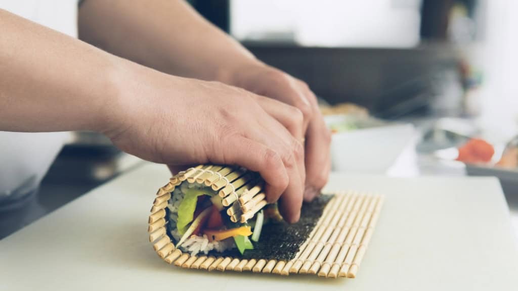 online-Kochkurs-Asien-Sushi-rollen Sushi wird in einer Sushi Rollmatte geformt.