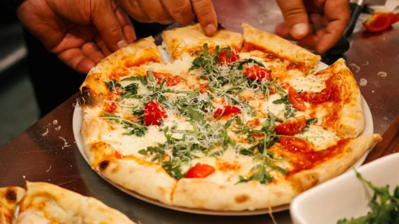 Drei Hände nehmen sich ein Stück einer Pizza.