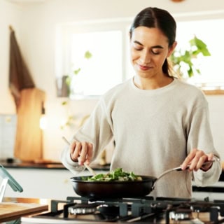 Eine Frau nimmt an einem Online Kochkurs teil und brät veganes Essen an.