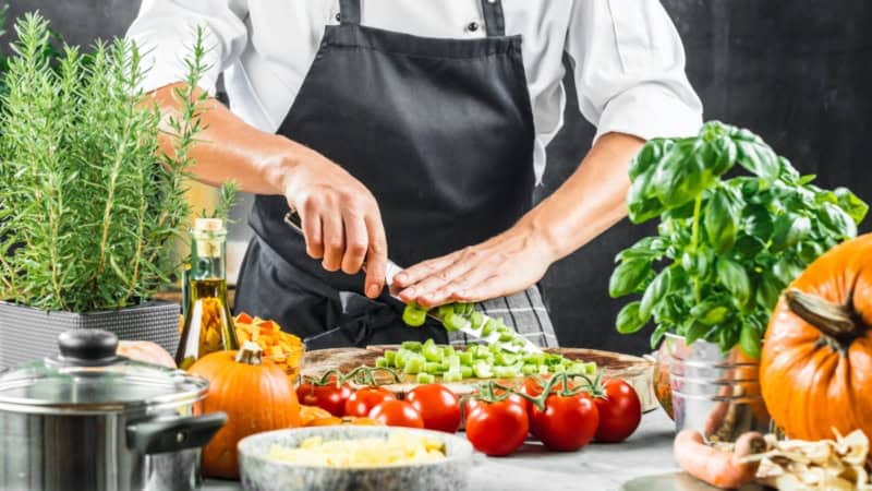 Lauch wird auf einem Tisch voller Gemüse von einem Koch geschnitten.