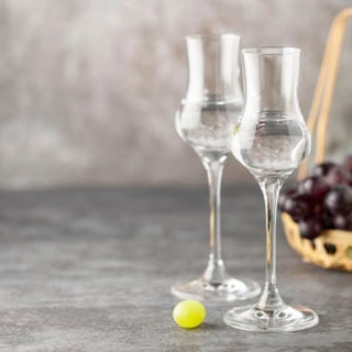 Auf dem Bild sind Gläser mit Schnaps und Trauben im Korb zu sehen.