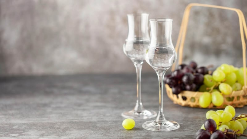 Auf dem Bild sind Gläser mit Schnaps und Trauben im Korb zu sehen.
