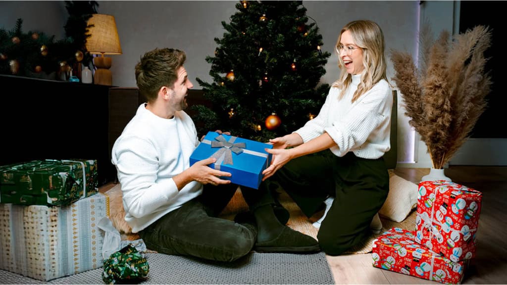 Eine Frau überreicht ein Erlebnisgeschenk an ihren Mann. Beide freuen sich