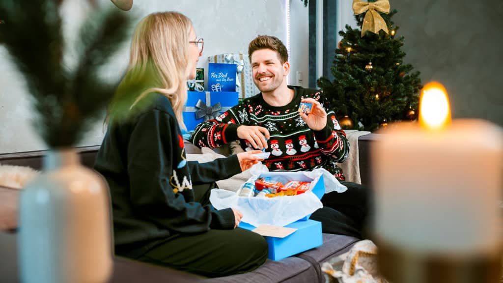 Ein Mann öffnet an Heiligabend mit seiner Frau die Trabi Geschenkbox der Erlebnisfabrik und freut sich.