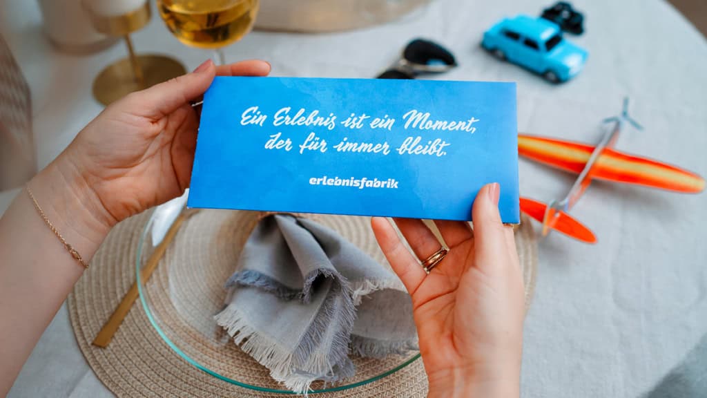 Gutschein - Weihnachten - ansehen Ein Gutschein der Erlebnisfabrik wird von einer Frau in beiden Händen gehalten und sich angeschaut.