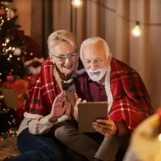 Ein Elternpaar sitzt zusammen am Weihnachtsbaum und telefonieren über ein Tablet.