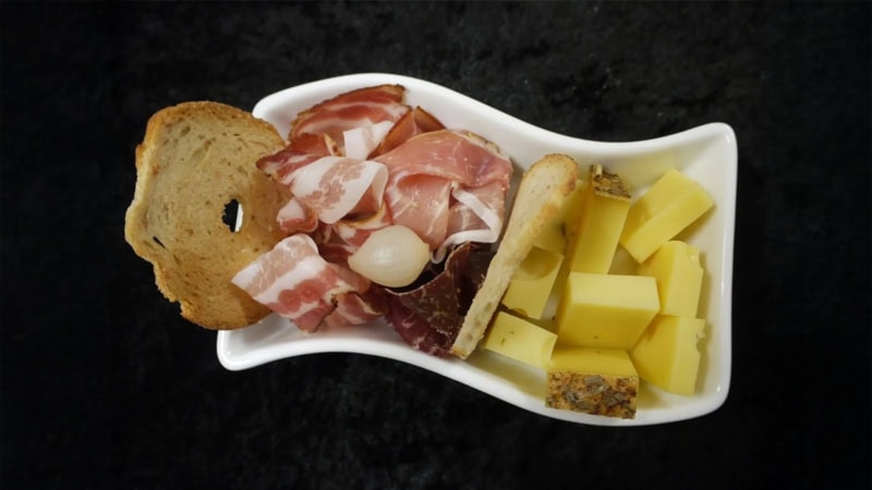 Vogelperspektive eines kleinen Tellers mit Käsewürfeln, Brotchips und Schinkenstücken.