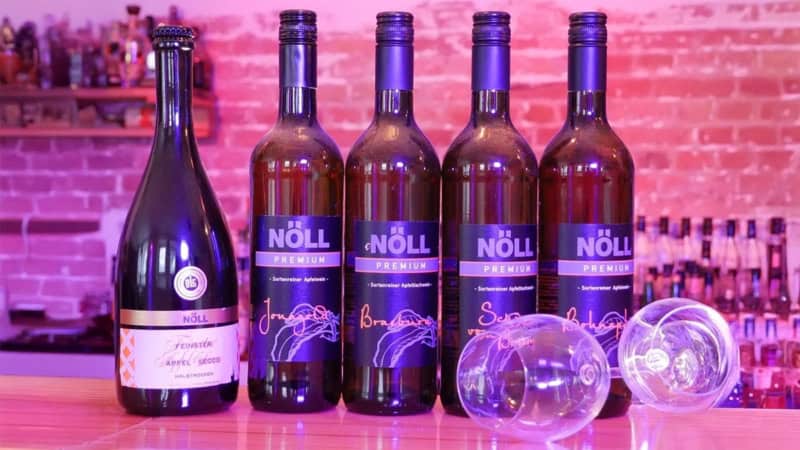 Eine Reihe von Apfelweinflaschen und ein liegendes Weinglas stehen auf einem farbig beleuchteten Bartresen.