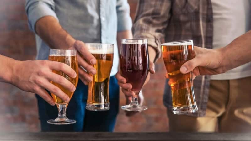 Vier Männer stoßen mit jeweils einem gefüllten Glas Bier an.