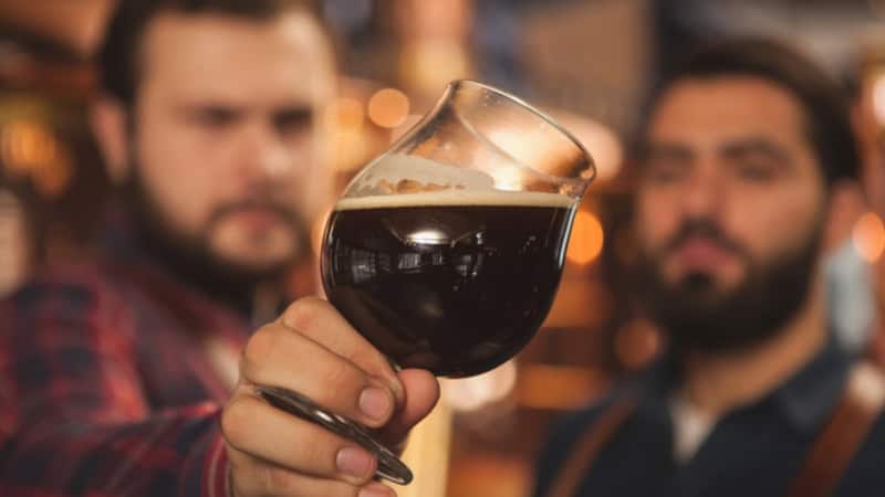 Zwei Männer inspizieren ein Glas mit dunklem Bier.