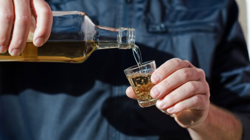 Mann im Hemd hat ein Shot-Glas in der Hand und füllt sich Chachaca ein.