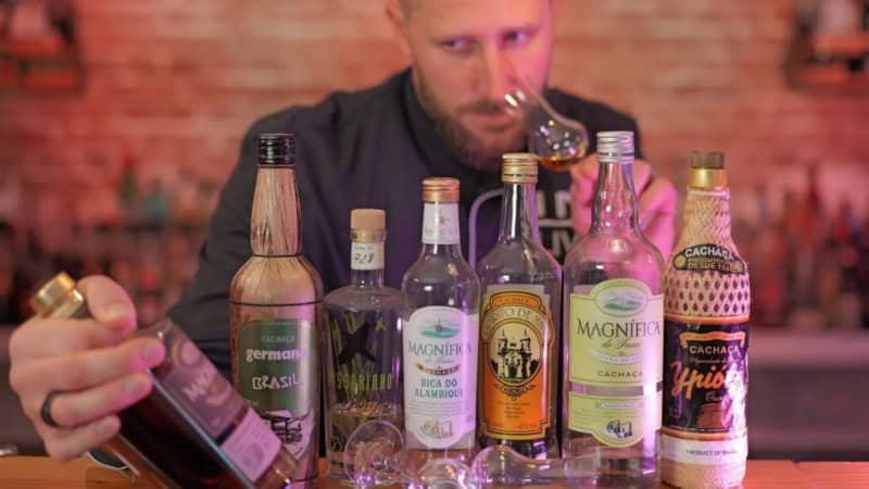 Barkeeper steht hinter der Bar und hinter aufgereihten Chachaca-Flaschen und riecht an einer Alkoholprobe.