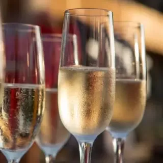 Mehrere mit Champagner gefüllte Sektgläser stehen vor einem dunklem Hintergrund.