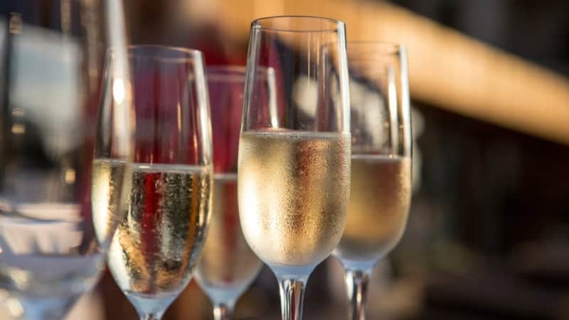 Mehrere mit Champagner gefüllte Sektgläser stehen vor einem dunklem Hintergrund.