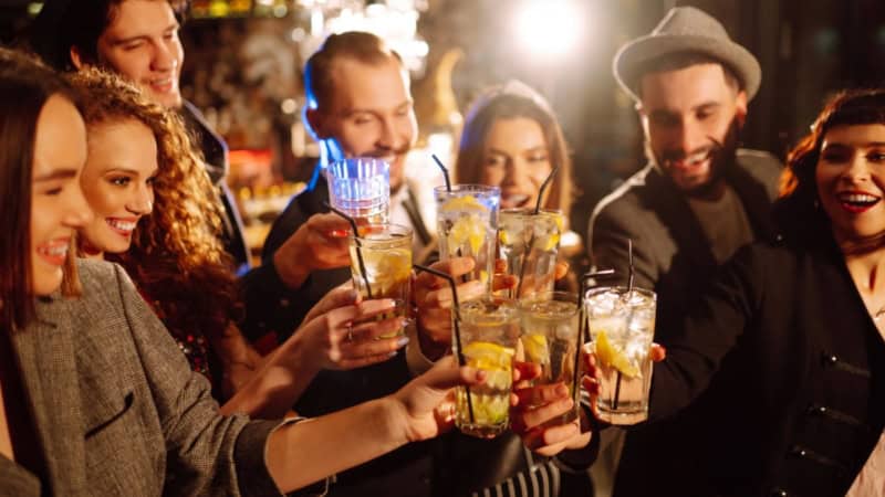 Eine Freundesgruppe stößt am Abend mit Cocktails in einer Bar an.