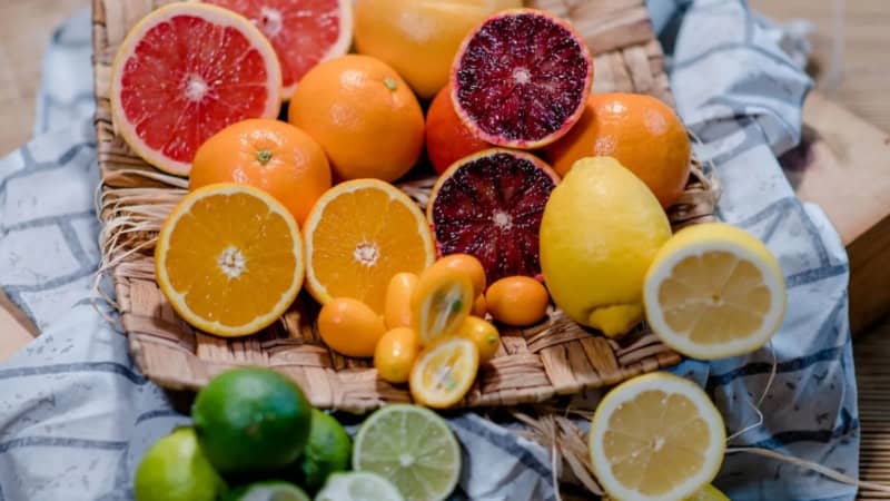 Verschiedene bunte Früchte wie Zitronen, Orangen, Limetten und Grapefruits liegen auf einer geflochtenen Unterlage auf einem Tuch.