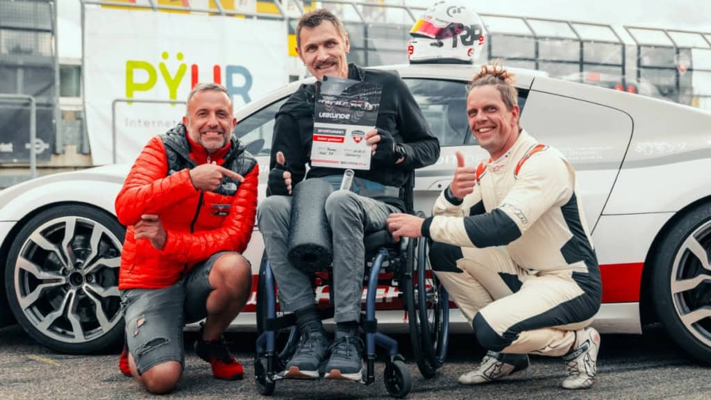 Handicap Fahrer mit Instruktoren vor einen Traumwagen bei der Urkundenübergabe