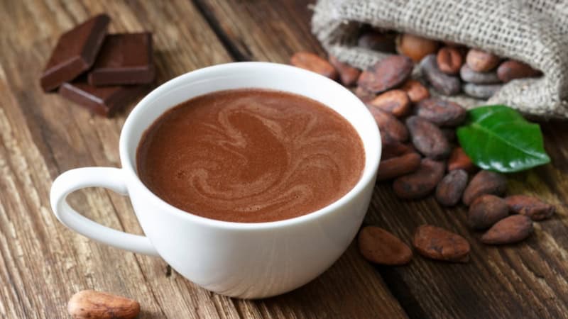 Kakao in einer Tasse neben einem Beutel Kakao Bohnen