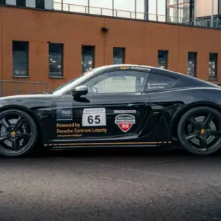 Porsche 718 GT4 in seitlicher Ansicht vor einem Gebäude bei der Rennstrecke.