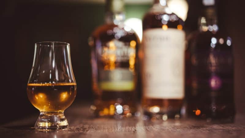 Ein befülltest Rum-Glas steht vor aufgereihten Rumflaschen auf einem hölzernen Bartresen.