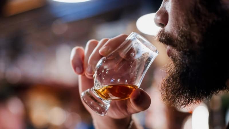 Mann mit Vollbart trinkt Rum aus einem kleinen Glas.