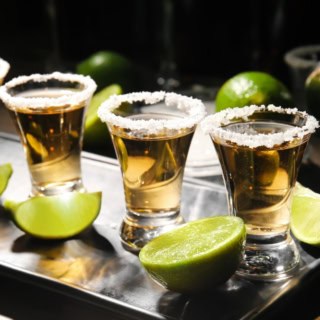 Tequila Shots stehen aufgereiht auf einer Unterlage. Daneben liegen Limetten.