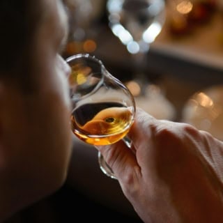 Mann sitzt an einem Esstisch und verkostet Whiskey aus einem Glas.