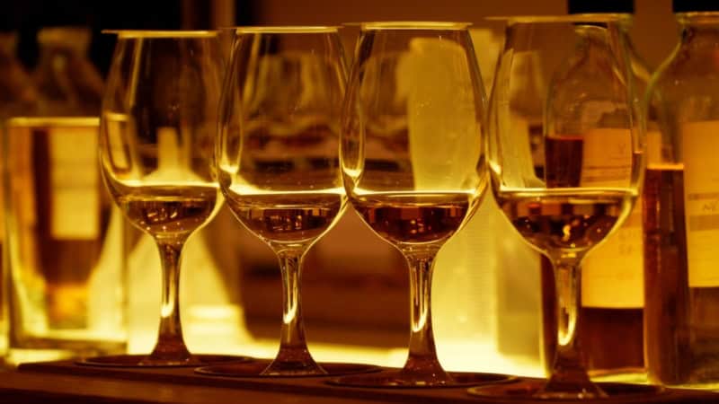 Whiskygläser stehen befüllt und golden beleuchtet aufgereiht auf einem Bartresen.