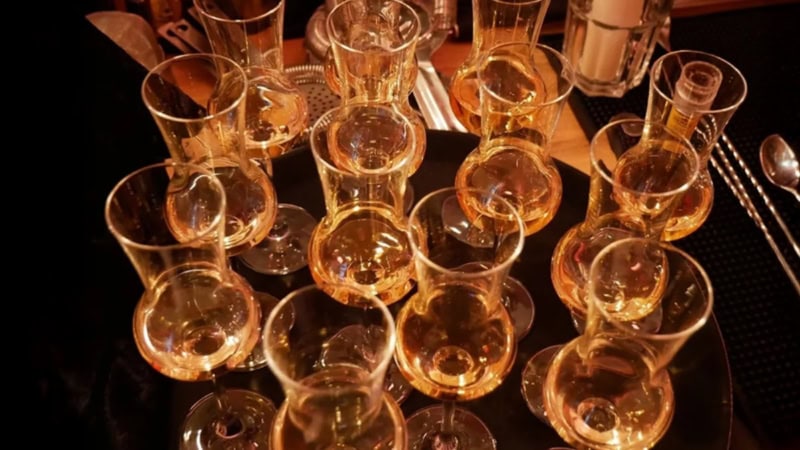 Viele orange beleuchtete und gefüllte Whiskeygläser stehen auf einem dunklen Bartresen.