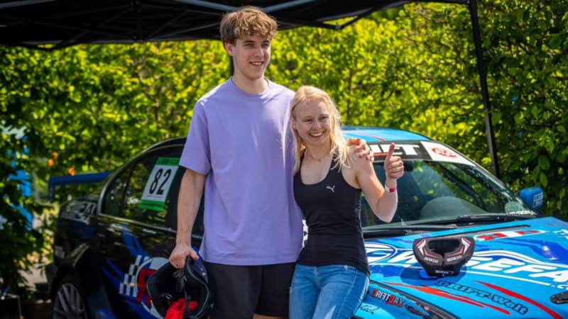 Ein Junge und ein Mädchen stehen zusammen an ein Sportauto gelehnt und freuen sich.