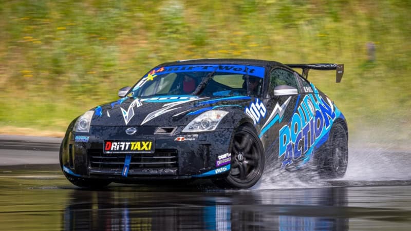 Ein schwarzes Sportauto mit blauen Details driftet über eine Nasse Rennstrecke am Nürburgring.
