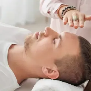 Ein Mann liegt auf einer Liege und eine Therapeutin hält ihre Hände über seinen Kopf und gibt ihm Energie.