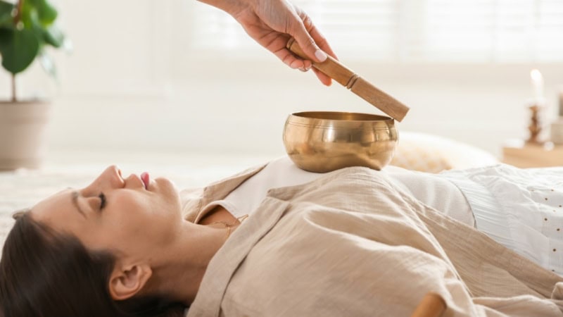 Eine Frau die mit einer Klangschale auf ihrer Brust behandelt wird.