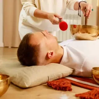 Ein Mann der mit einer Klangschale auf seiner Brust behandelt wird.