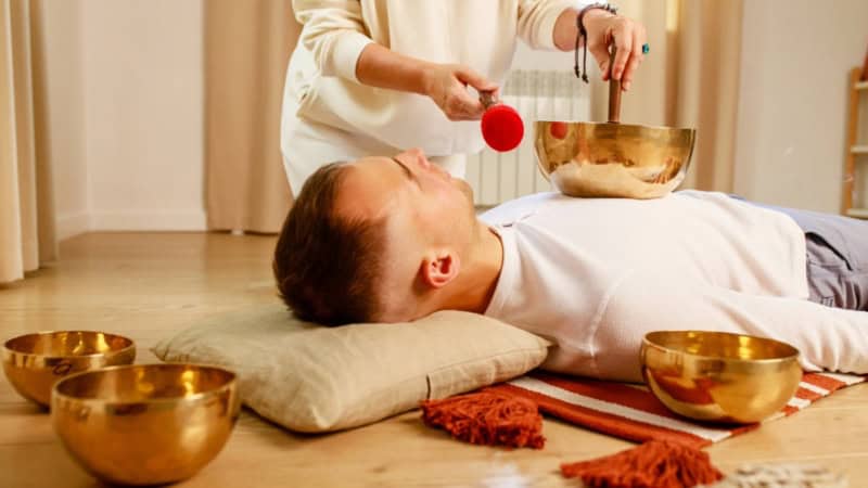 Ein Mann der mit einer Klangschale auf seiner Brust behandelt wird.