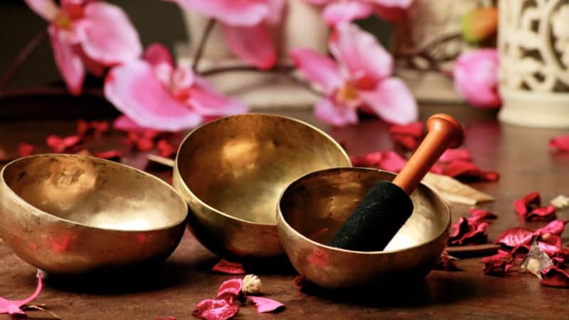 3 Klangschalen die zwischen Blumen liegen.