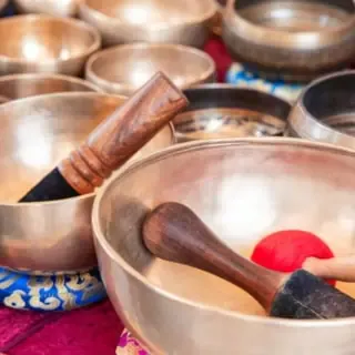 Viele verschiedene Klangschalen die auf Kissen stehen.