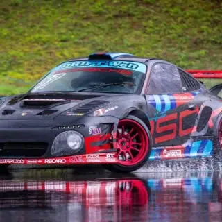 Ein schwarzes Sportauto von Porsche driftet über nassen Asphalt auf dem Nürburgring.