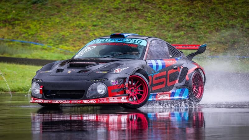 Ein schwarzes Sportauto von Porsche driftet über nassen Asphalt auf dem Nürburgring.
