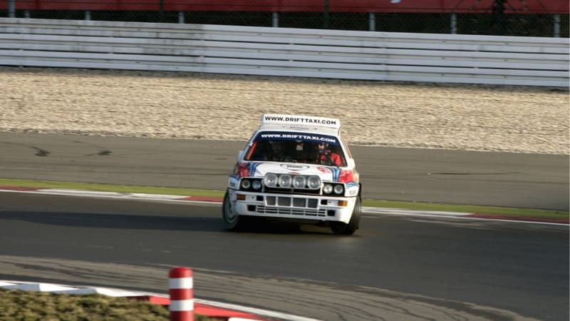 Ein weißes Auto driftet in einer Kurve der Rennstrecke des Nürburgrings.