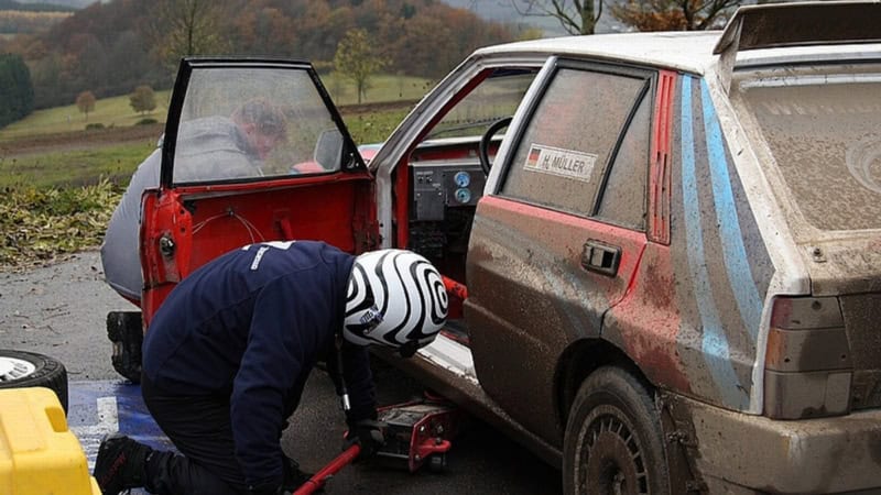 Zwei Fahrer überprüfen und reparieren ein dreckiges Auto am Straßenrand.