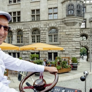 Guide auf einer e-Kutsche in den Straßen von Leipzig, auf einer Rundfahrt vor einem Historischen Gebäude.