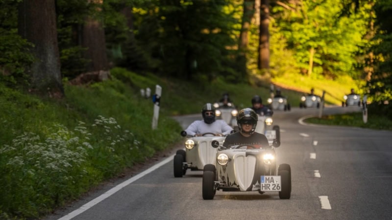 Hotrod Fahrer einer Hotrod Tour die in einer Reihe auf einer Straße durch den Wald fahren.