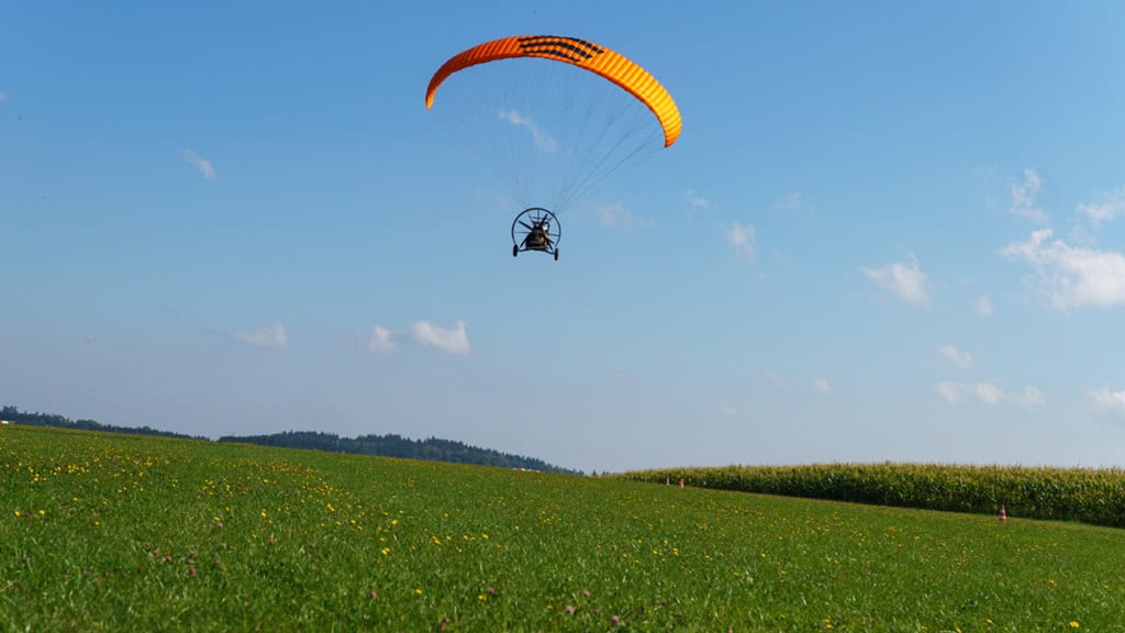 motorisierter-Gleitschirmflug-sachsen7 Trike ist in der Luft und gerade bei der Landung. Unten Wiese oben Himmel.