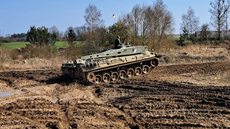 Ein Panzer der über ein Schlamm Feld fährt.