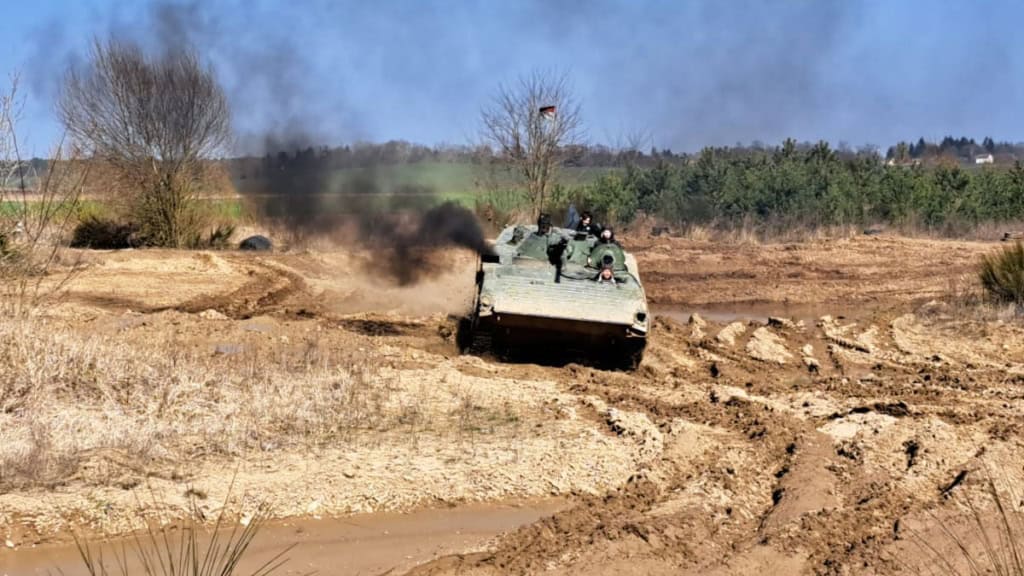 Panzer-fahren-bei-Berlin-kurve Ein Panzer der durch Matsch fährt und eine große Rauchwolke ausstößt.