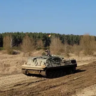 Ein Mann der mit einem Panzer über einen Matsch Weg fährt.