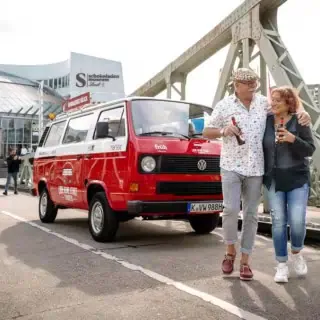 Ein Paar steht vor einem VW Bulli der vor dem Schokoladenmuseum im Köln steht.